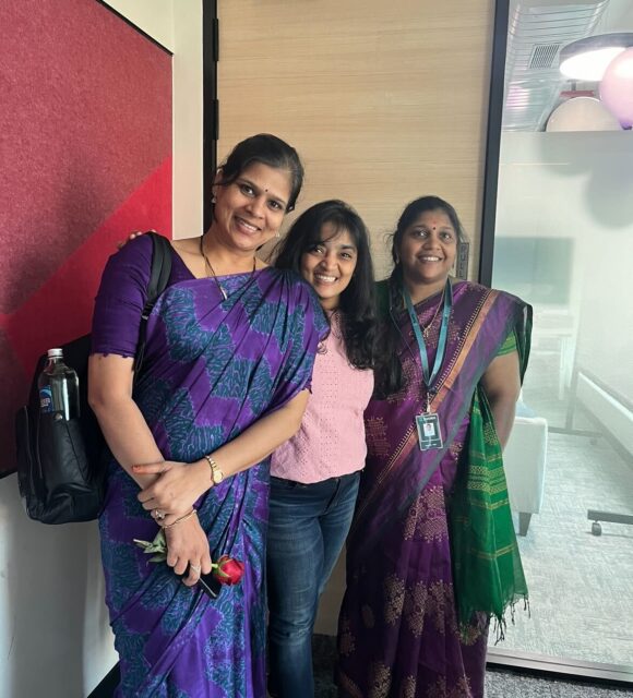Three women in purple saris posing for a photo.