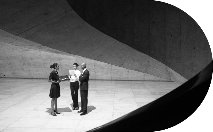 Three people engaged in conversation inside a modern structure with curved concrete walls.
