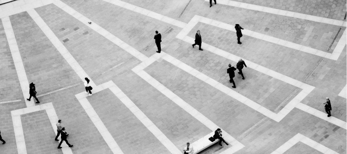 An overhead black and white shot of people walking across a patterned square.