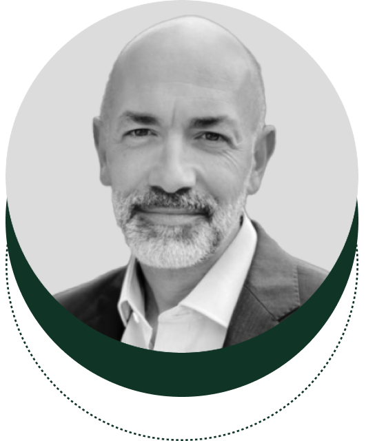 A grayscale headshot of a bald man with a beard, dressed in a suit, enclosed within a circular green border.