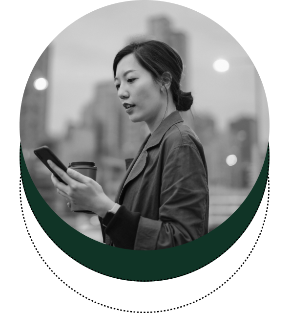 A woman in a leather jacket holding a coffee cup and looking at her smartphone, with a cityscape in the background.