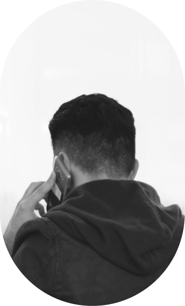 A person with short dark hair, wearing a hoodie, faces away and holds a phone to their ear.