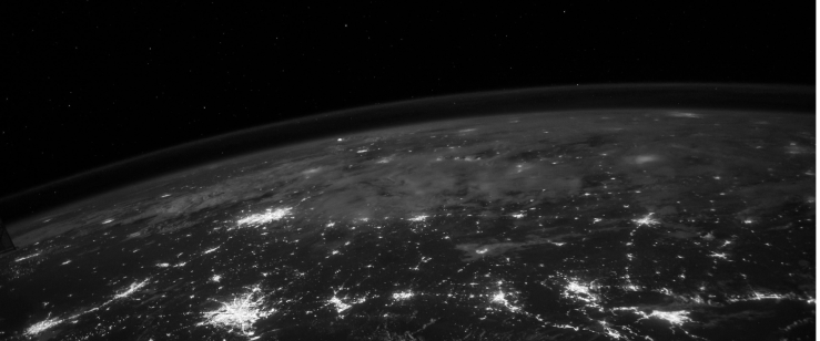 Black and white view of Earth from space showing illuminated cities at night under a star-filled sky.
