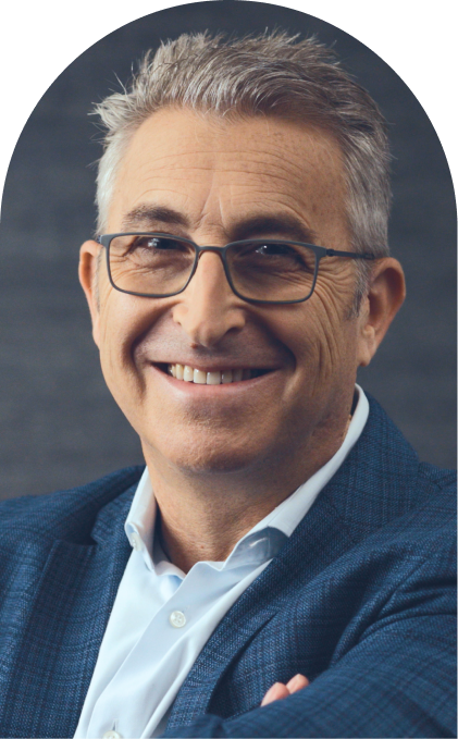 A smiling man with short gray hair and glasses is wearing a blue blazer and a light blue shirt, posing against a dark gray background.