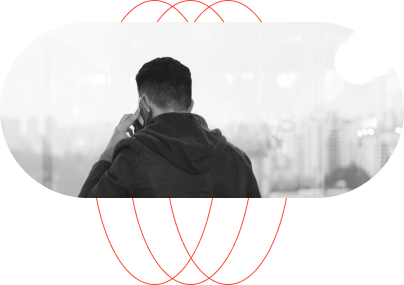 A person wearing a hoodie is seen from behind, talking on a phone while looking out at a cityscape through a window.