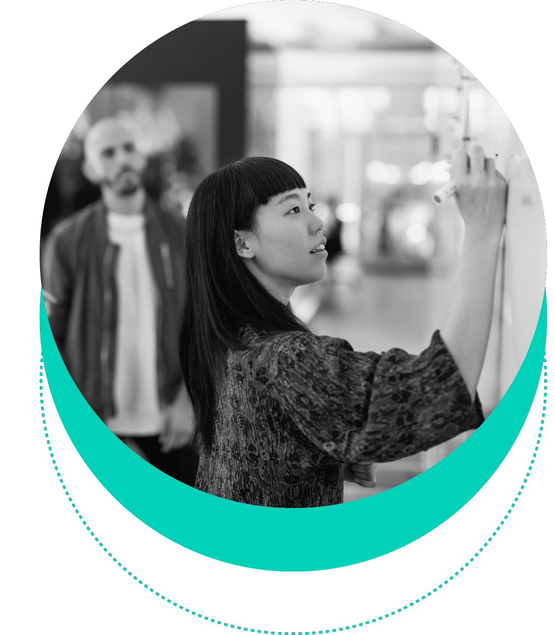 A person with long hair writes on a whiteboard while another individual stands in the background watching.