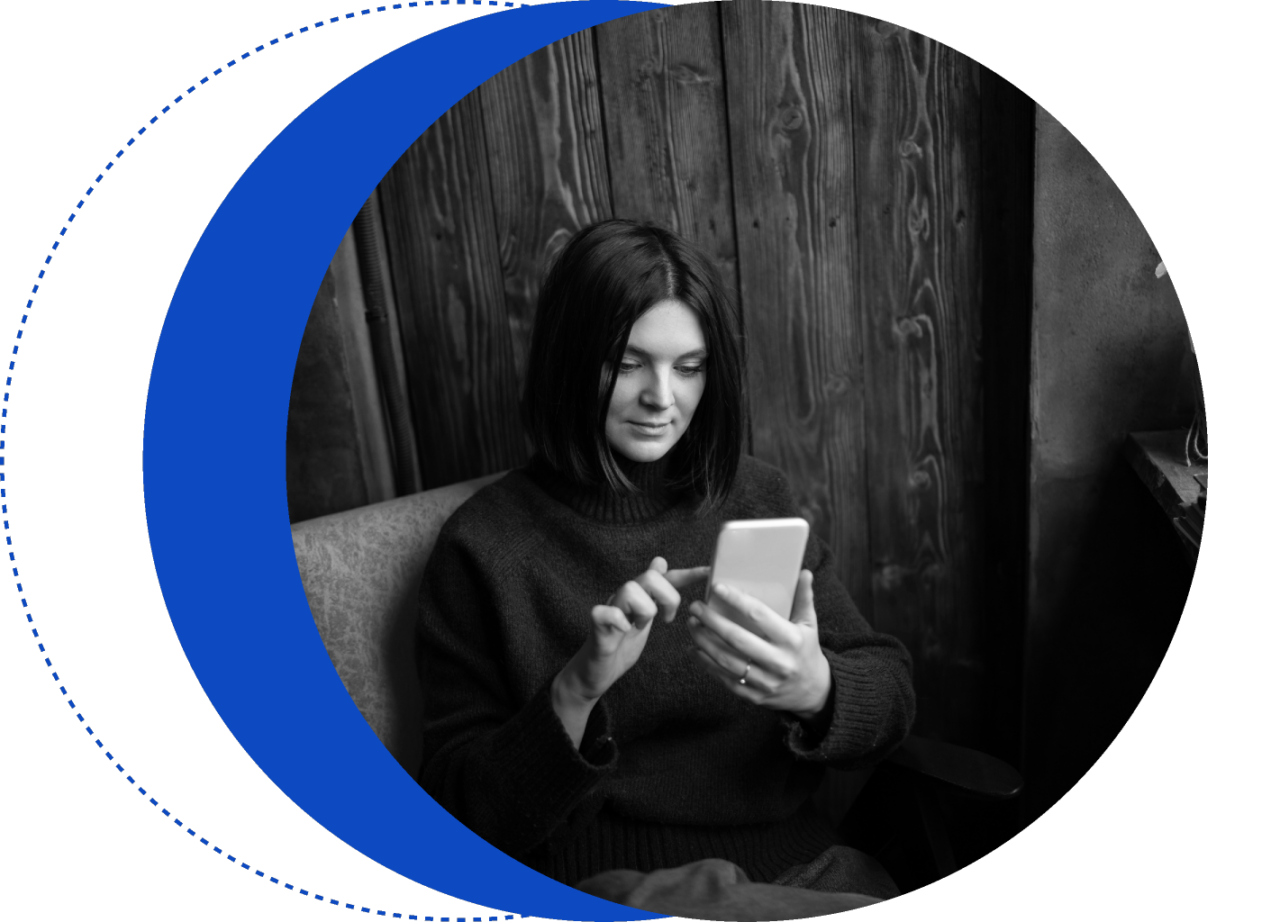 椅子に座ってスマートフォンを見ている人物。肩までの長さの髪をしており、黒いセーターを着ている。画像は白黒で、左側に青い三日月形が描かれている。