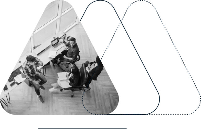 オフィス環境では、車椅子を使用する人も含め、数人の人々が共同作業を行っています。彼らは、コンピューター、書類、その他の事務用品が置かれた机の周りに集まっています。