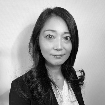 長い黒髪の人物がブレザーと白いトップスを着て、無地の背景に日本の優雅さを体現した白黒ポートレート。