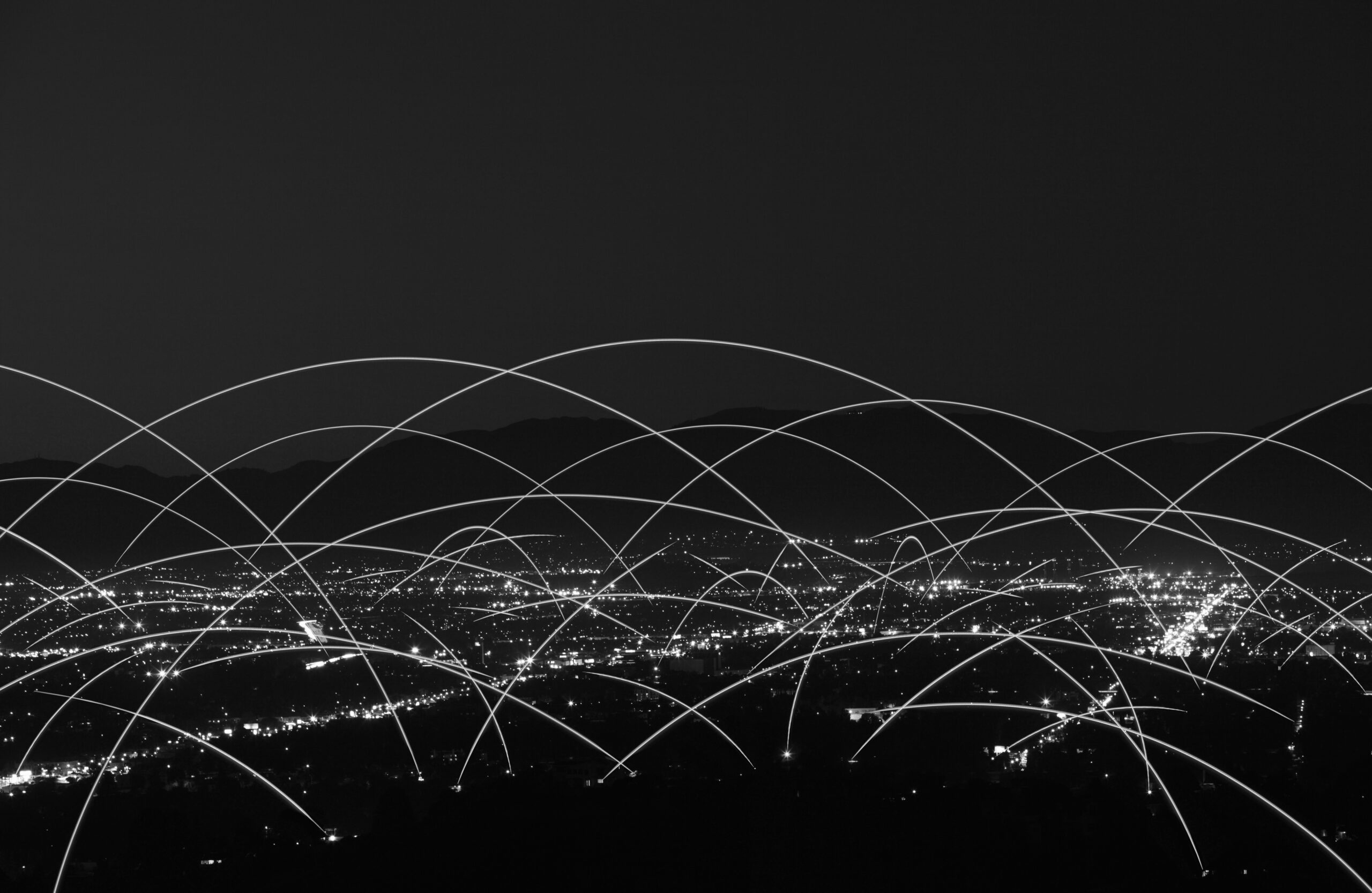 A cityscape at night with white light trails arching over the skyline, representing digital or wireless network connections.