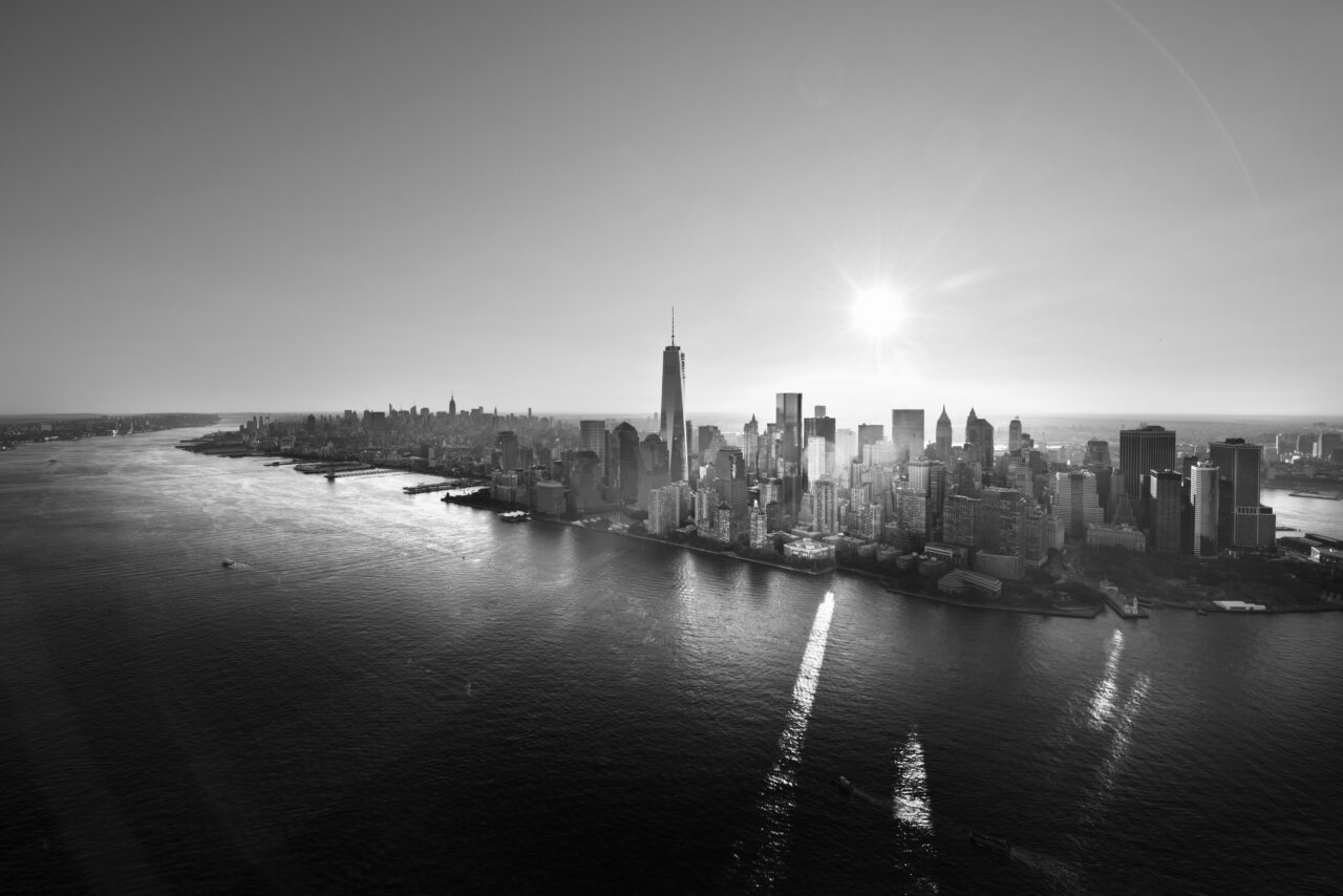 Aerial view of lower Manhattan, New York City, with the sun shining above the skyline and reflecting on the water.