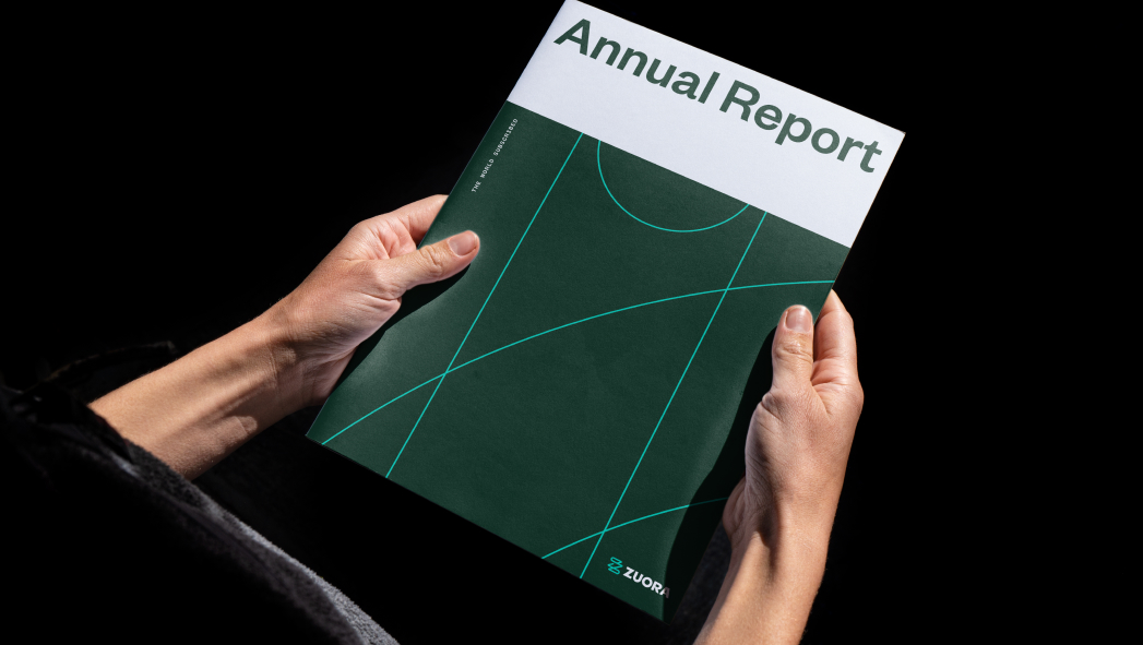 A person holds a brochure titled "Annual Report" with a green geometric cover design against a black background.