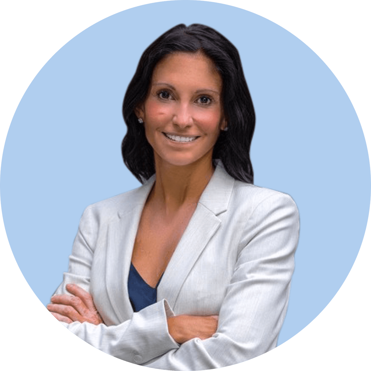 Woman with long dark hair wearing a light gray blazer and navy shirt standing with arms crossed, smiling, in front of a light blue background.