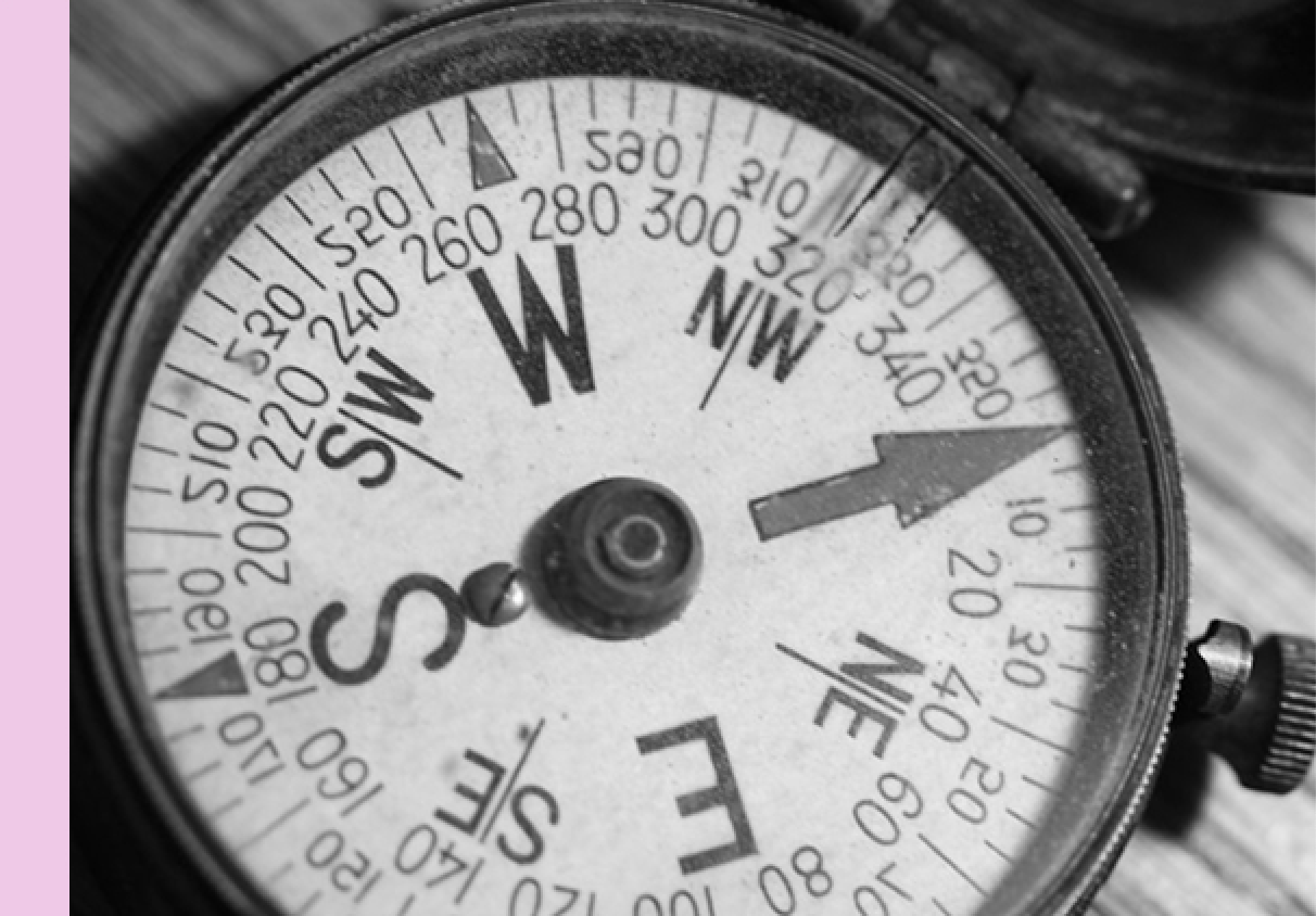 A close-up, black-and-white photo of an analog compass with cardinal directions and degree markings visible, symbolizing strategy and guidance.