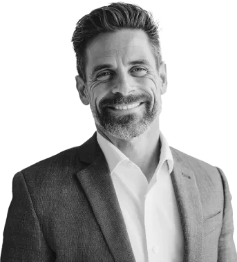 A man with short hair and a beard, wearing a suit jacket over a white shirt, smiling at the camera.