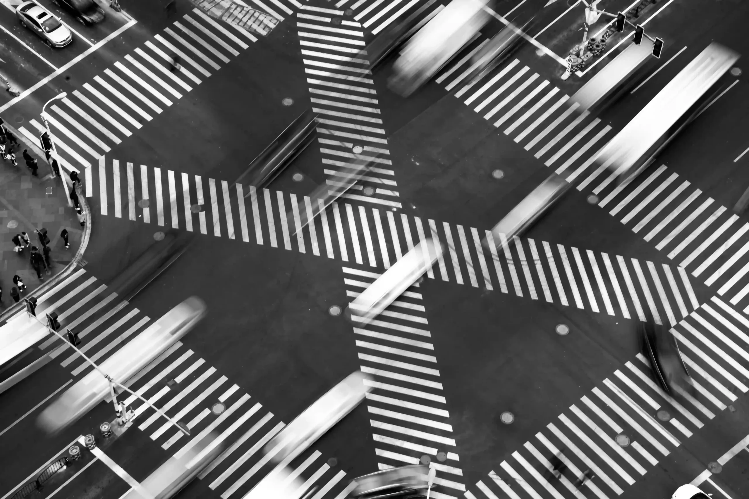 Aerial view of a busy intersection with diagonal crosswalks, blurred motion of cars and people, black and white.