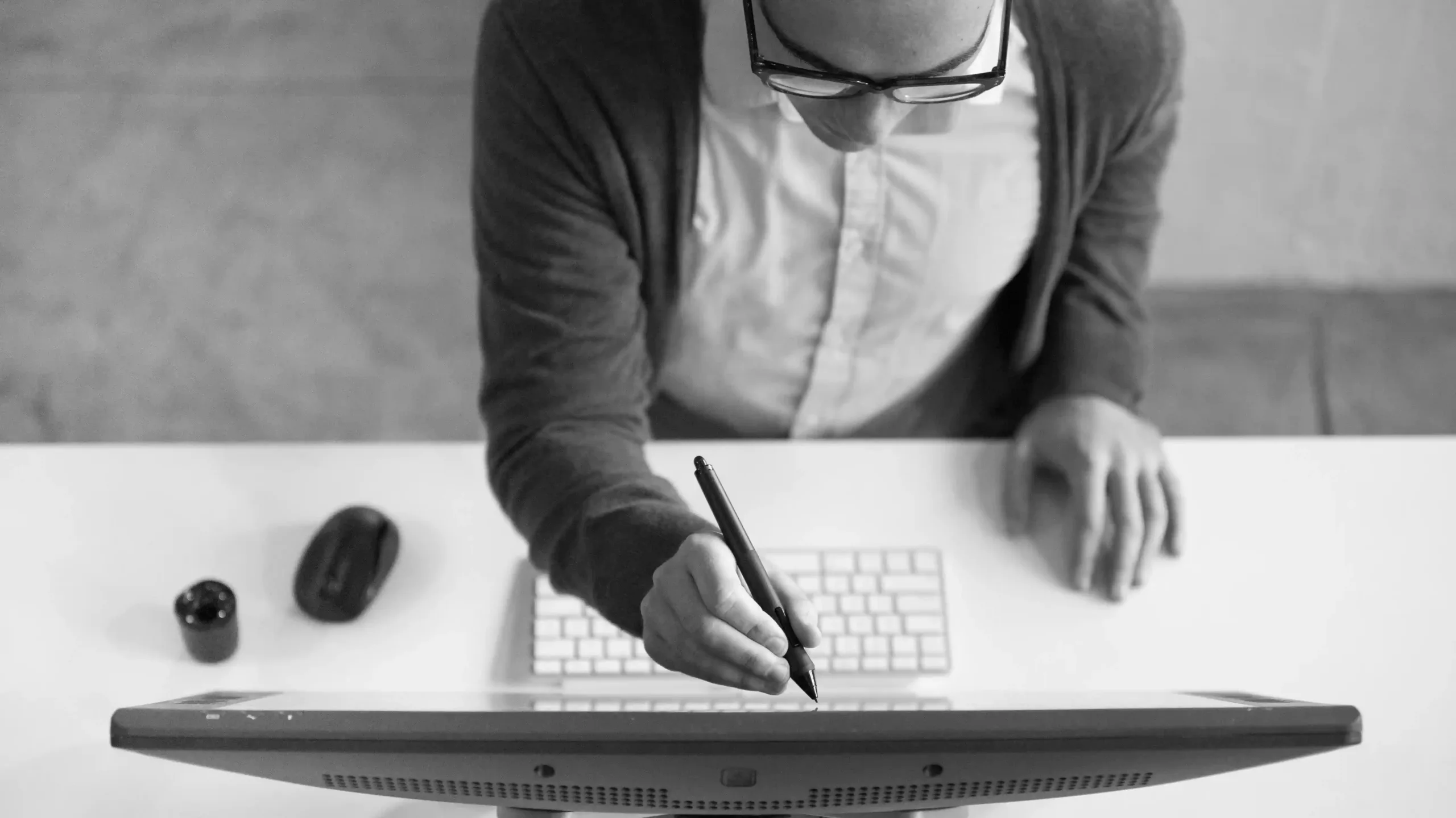 A person uses a stylus on a graphic tablet while sitting at a desk with a keyboard and mouse, viewed from above.