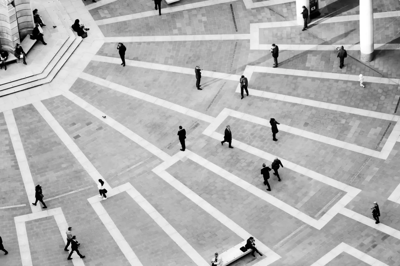 Aerial view of people walking and standing on a geometric patterned plaza with intersecting straight lines and rectangular tiles.