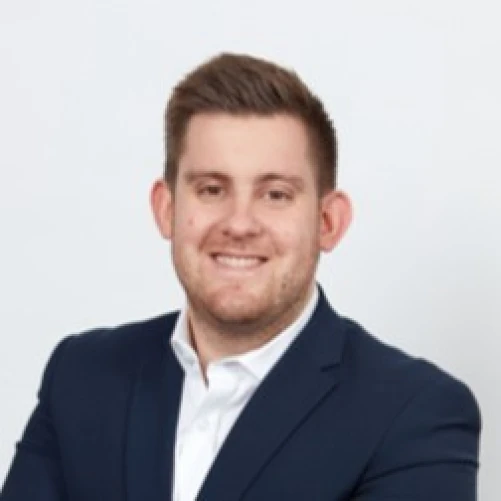 A man in a dark suit jacket and white shirt is smiling at the camera, posing against a plain white background.
